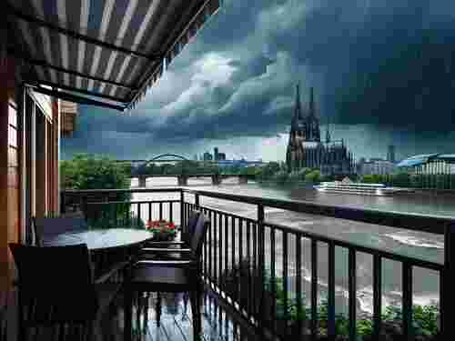 Markise auf einem Balkon bei Regen und dunklen Wolken mit Blick auf den Kölner Dom und den Rhein.