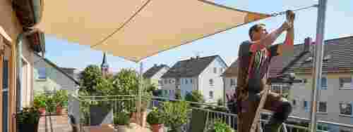 Professioneller Monteur spannt eine Sonnensegel-Markise über einer Terrasse in Lohmar, Stadtblick