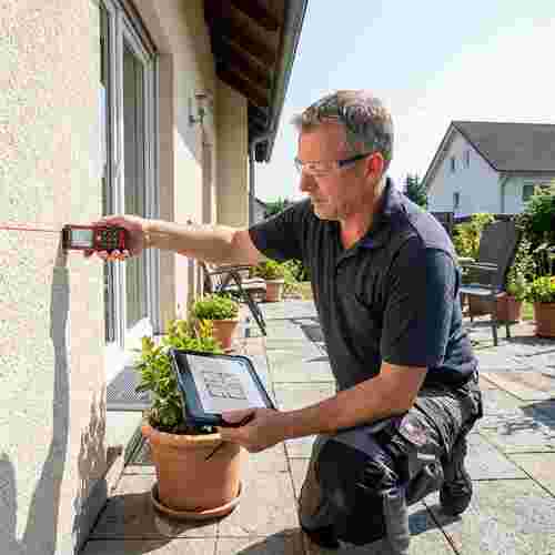 Techniker vermisst Sonnenschutzmontage auf Terrasse mit Laserentfernungsmesser und Tablet